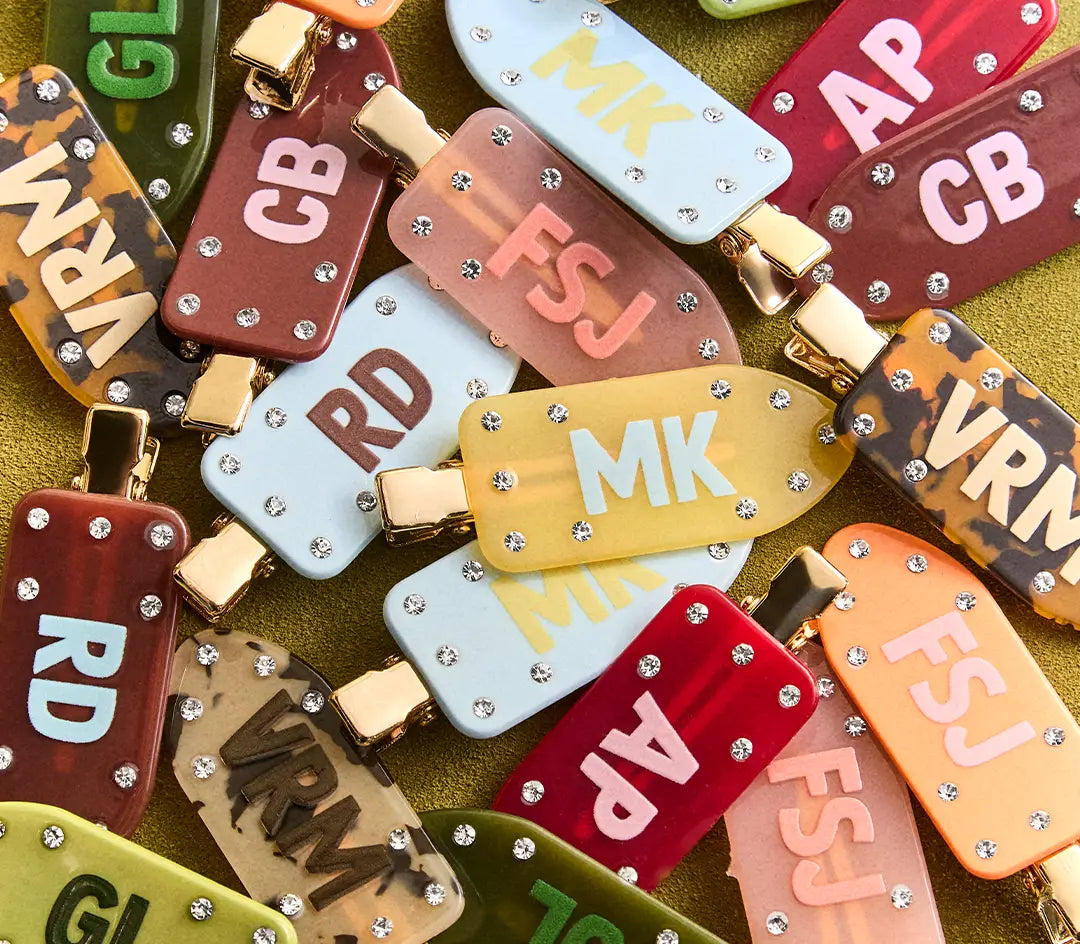 Pile of colorful popsicle-shaped hair clips with crystal studs and monogram initials such as MK, CB, FSJ and RD.