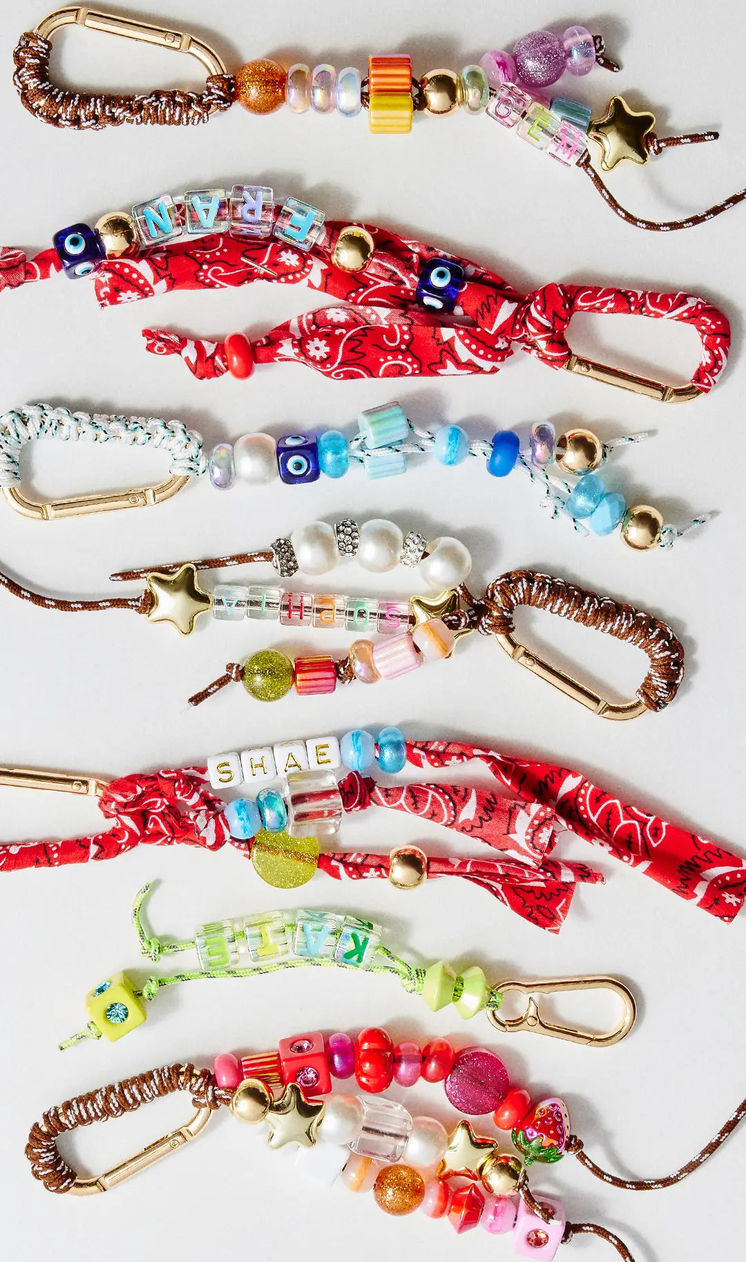 Beaded carabiner bag charms with letter beads spelling “GEM,” “FRAN,” “SOPHIA,” “SHAE” and “KATE,” with pearls, gold stars and bandana ties.