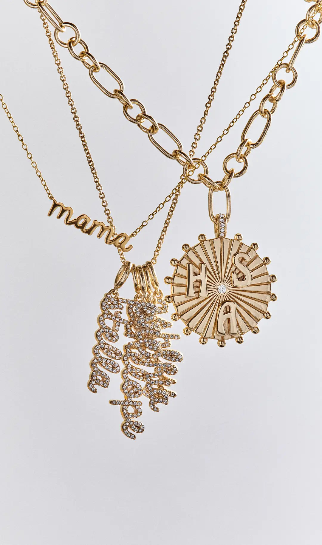 Gold necklaces including a “mama” script nameplate, a cluster of crystal script name charms and a sunburst medallion with the letters H, S and A.