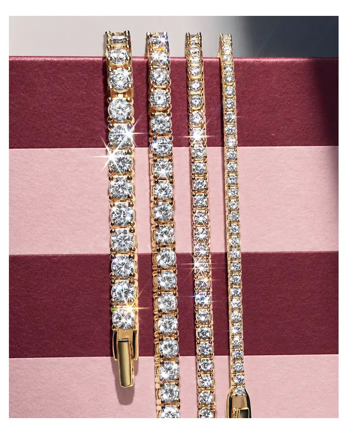 Four gold crystal tennis bracelets in graduated widths hang against a burgundy-and-pink striped box.