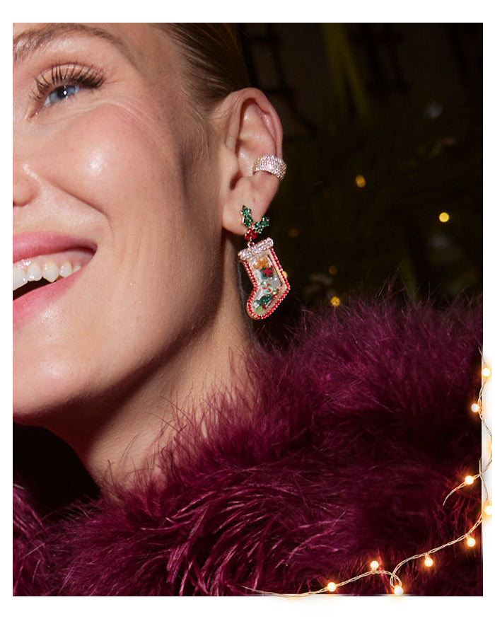 Smiling woman in a plum feather wrap wears a crystal ear cuff and a beaded Christmas stocking drop earring with holly.