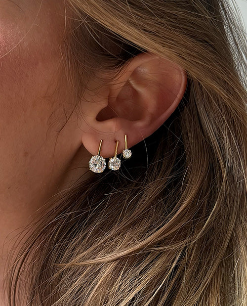 Close-up of a person's ear wearing three gold hoop earrings with round clear gemstones of varying sizes.