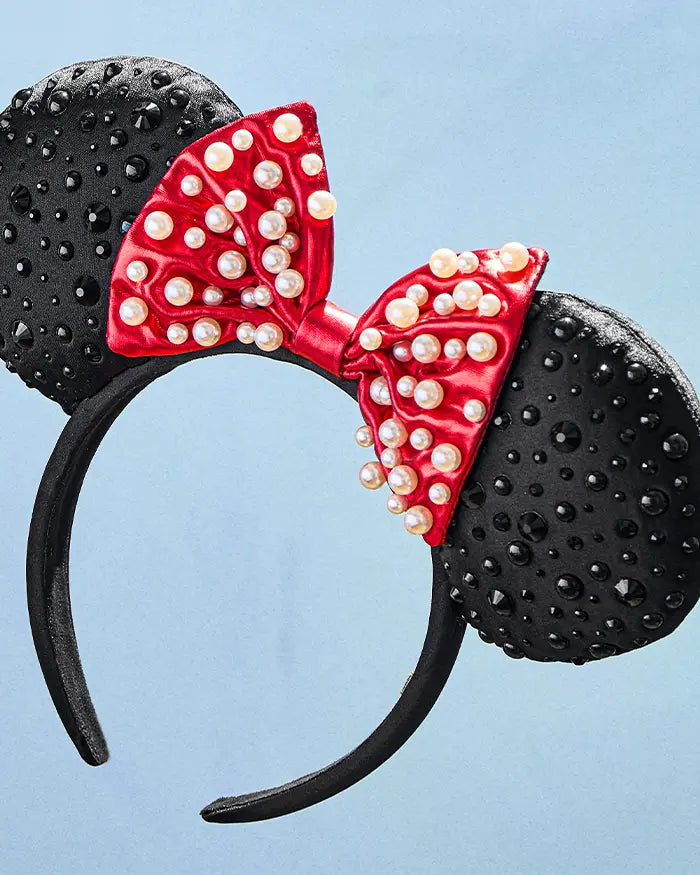 Black ear headband studded with crystals, topped with a red satin bow covered in pearls.